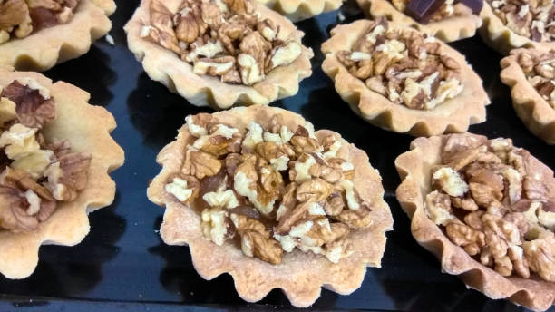 istock Homemade shortcake pastry tartlets. Shortcrust baskets with nuts on a black baking tray. Tartlets made from shortcrust pastry with nuts & applesauce. 1221254879