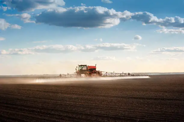 Photo of self-propelled sprayer with long arms disperses fertilizers on agricultural fields, rear view, backlit jet