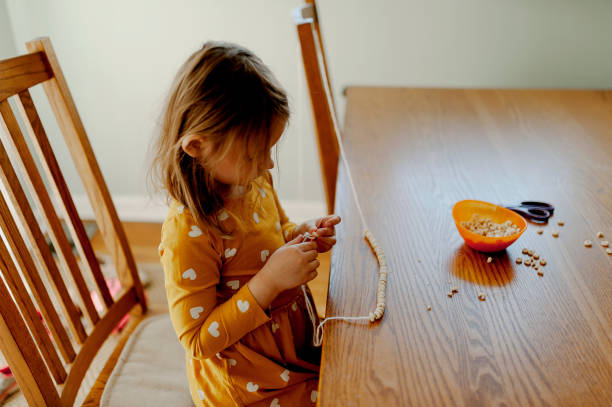 little girl stringing cereal onto a string to make a cereal necklace or garland - 4 string imagens e fotografias de stock