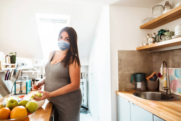 donna incinta che cucina con maschera facciale durante la quarantena - mother emotional stress exhaustion cooking foto e immagini stock