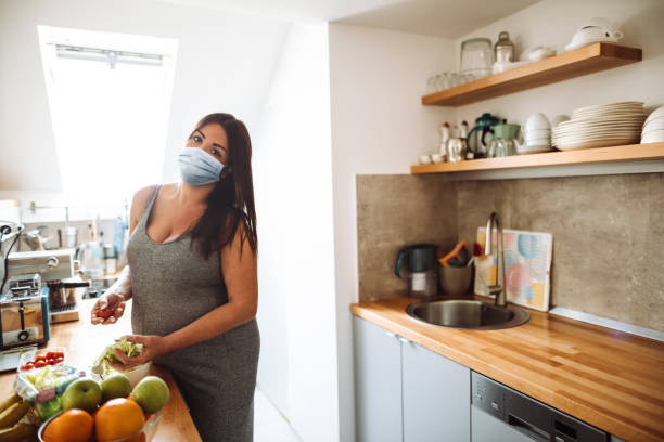 donna incinta che cucina con maschera facciale durante la quarantena - mother emotional stress exhaustion cooking foto e immagini stock