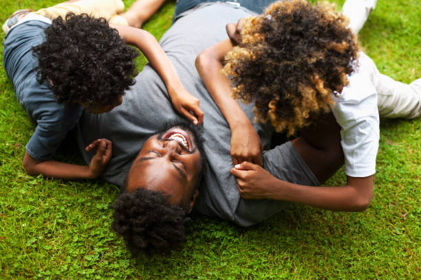 African-American father playing with two sons laying on grass