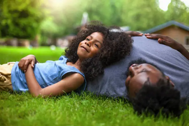 Photo of African-American son and father rests on grass at backyard holiday villa