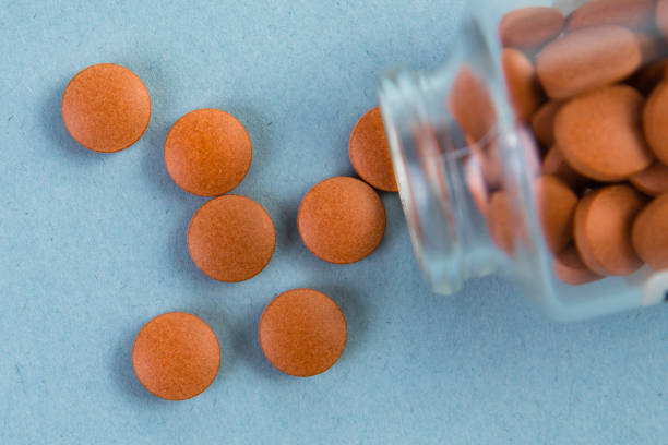 istock Glass bottle, with orange pills spilling out on a blue background 1221267314