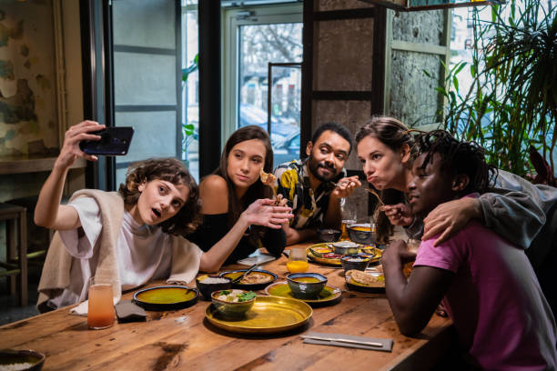 istock Five young friends sitting at the table in a cafe, taking selfies, having a nice time 1221270261