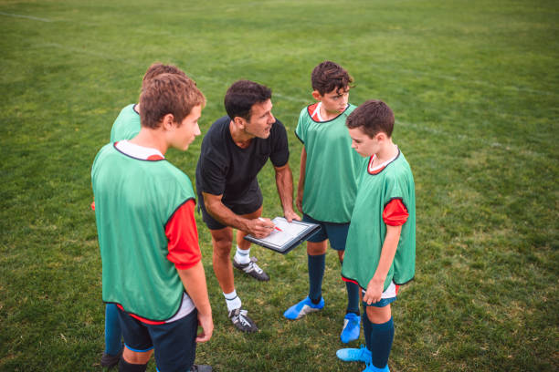 istock Coach Sketching Play Notes for Boy Footballers On Field 1221278010
