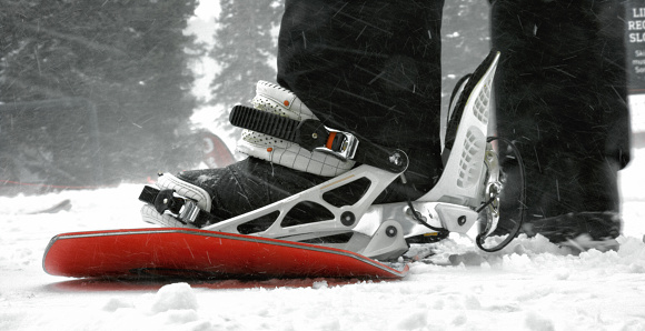 A Snowboarder Putting Their Booted Foot into the Bindings of a Snowboard at Eldora Ski Resort Near Boulder, Colorado on a Snowy, Overcast Day in Winter