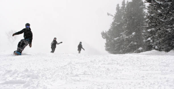 Three Snowboarders Boarding Down a Run at Eldora Ski Resort near Boulder, Colorado on a Snowy, Overcast Day