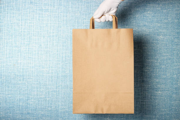 istock A woman's hand in white glove holds cardboard bag, against a blue background 1221287639