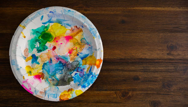 Colorful artist palette, made up of disposable white paper plate, on a wooden table