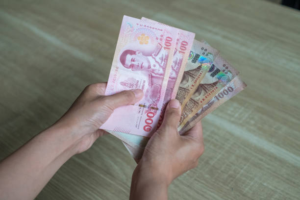 istock Thai money in hand for saving on wood background 1221296282