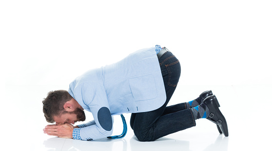 Profile view of aged 30-39 years old caucasian young male businessman kneeling in front of white background wearing jeans