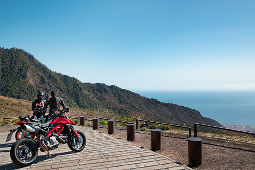 TF-523 Road or Carretera Los Loros, Tenerife, Canary Islands, Spain - March 12, 2020: two young male motorcyclists stopped at the viewpoint Mirador de Chivisaya to rest and enjoy the panoramic views.