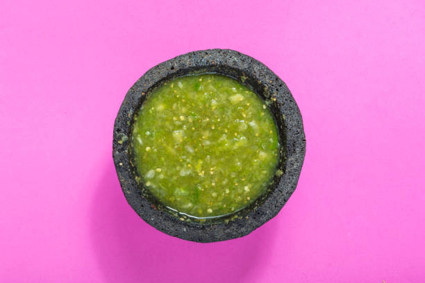 Raw salsa verde ingredients, Mexican food, green sauce Raw salsa verde ingredients, Mexican food. Tomatillos, onion, garlic, chili peppers and cilantro crushed in a molcajete. Green ingredients on pink background. tomatillo photos stock pictures, royalty-free photos & images