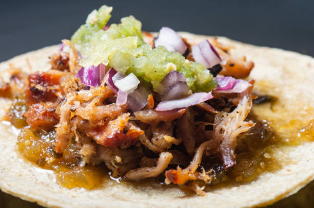 Carnitas tacos with raw salsa verde, Mexican food Carnitas tacos with red onion and raw salsa verde. Mexican slow cooked pork dish isolated on black plate tomatillo photos stock pictures, royalty-free photos & images