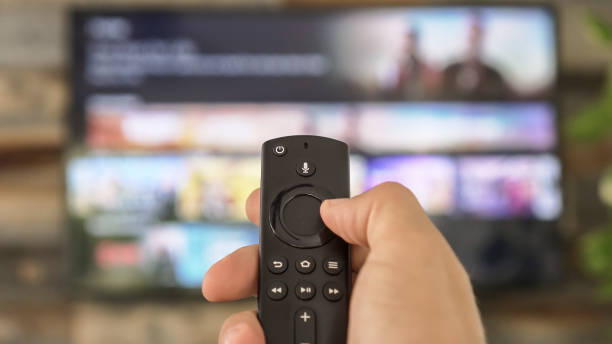 mano masculina sosteniendo el mando a distancia del televisor y cambiando los canales de tv. navegación por canales, centrada en la mano y el control remoto. televisión por internet. - remote area fotografías e imágenes de stock