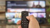 Male hand holding the TV remote control and changing TV channels. Channel surfing, focused on the hand and remote control. Internet TV.