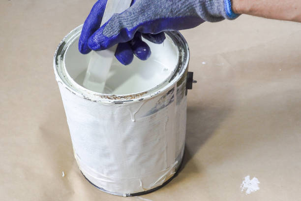 primo passo del pittore guantato a mano che mescola vernice in lattite di vernice metallica con bastone di legno. - paint mixing stick foto e immagini stock