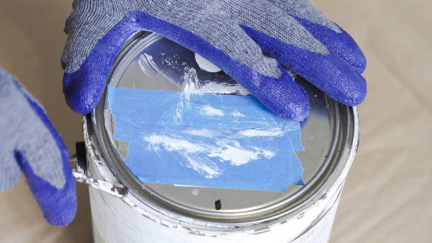 gloved hand opening a can of white paint with can opener before starting a paint room. - paint preparation adhesive tape indoors imagens e fotografias de stock