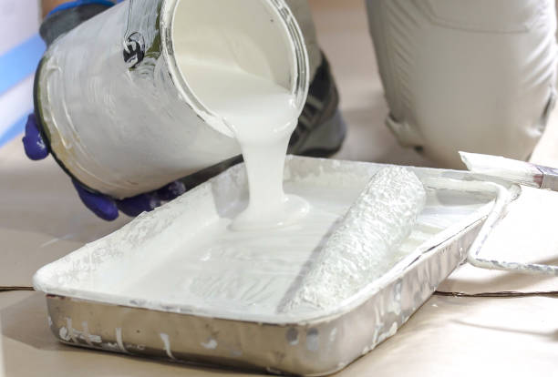 istock Man pours paint into the tray and dips roller. Professional interior construction worker pouring white color paint to tray. 1221306294