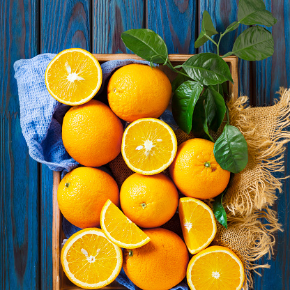 Close up of oranges on a blue kitchen towel with green leaves. Still life