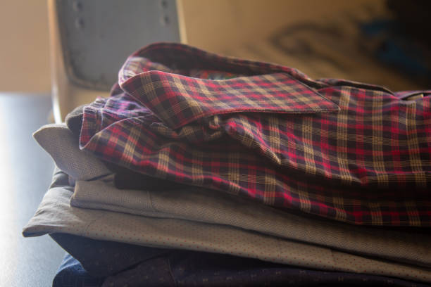 View of the folded shirts stacked over one another after ironed with Iron box in background.