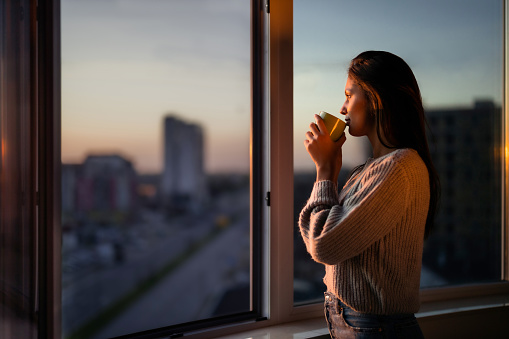 Vista de perfil de una hermosa mujer bebiendo café junto a la ventana. photo