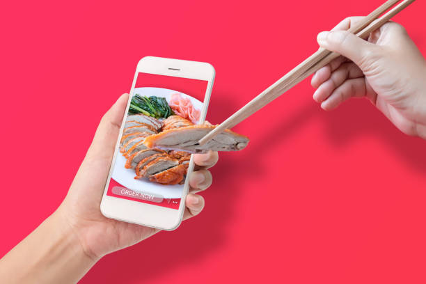 istock hand using chopsticks to clamp the roasted duck from application to made order food online via mobile smartphone, isolated on red background. online food order and delivery service advertise concept. 1221317511