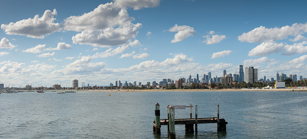 panorama showing the City of Melbourne on the horizon seen from St Kilda pier looking over old timber pylons in the bay or cove on a summer day, Victoria, Australia