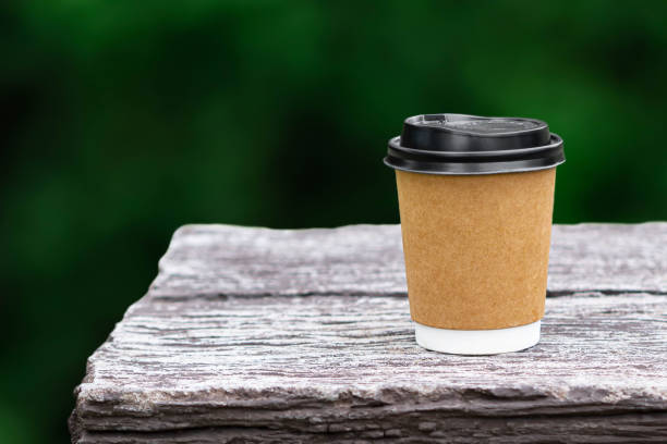istock Disposable coffee paper cup mockup on stone table with nature green blurred background 1221323606