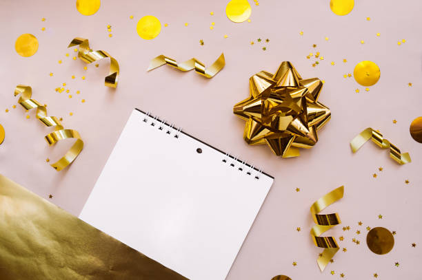 istock Spiral notebook with white clean pages on a soft pink background with gold decorations, sequins, stars, foil ribbons and a large gold bow for packaging. A festive layout for the content 1221324316