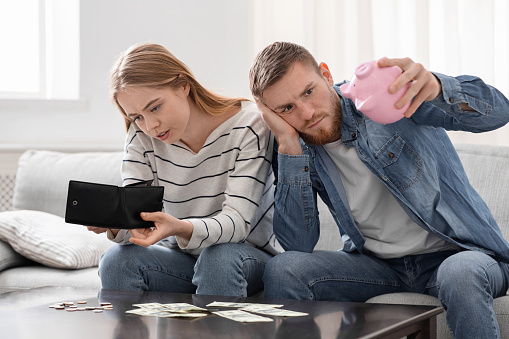 Coronavirus crisis. Desperate couple counting last money savings at home, looking at empty wallet and piggybank
