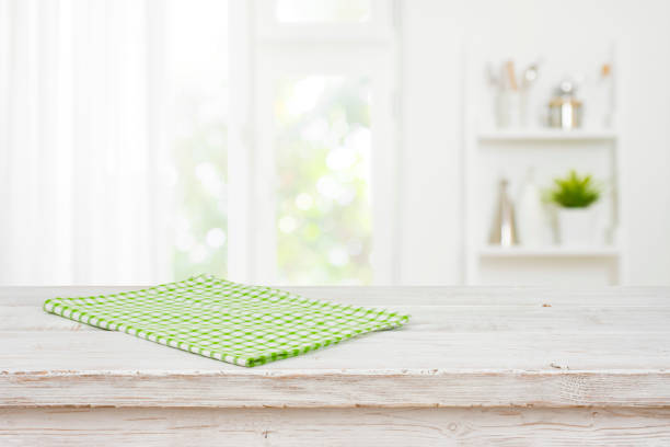Green kitchen towel on wooden table over blurred window background