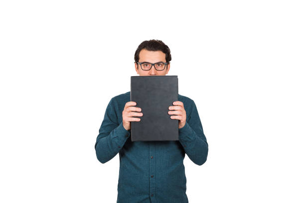istock Introvert businessman looking to camera, covers his mouth using briefcase, hiding facial expression, isolated on white background. Business worker holding a black case portfolio, wearing glasses. 1221344116