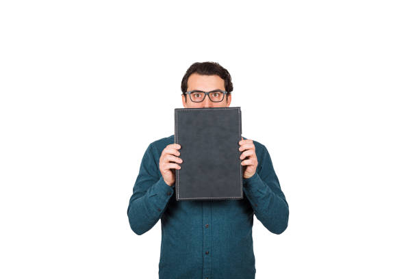 istock Shocked businessman looking astonished with big eyes, covers mouth using briefcase, hiding facial expression, isolated on white background. Business worker holding a black portfolio, wearing glasses. 1221344489