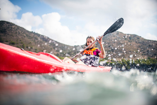 Low angle action close-up of fit Spanish female in late 20s paddling single kayak in Mediterranean Sea off the Costa Brava.