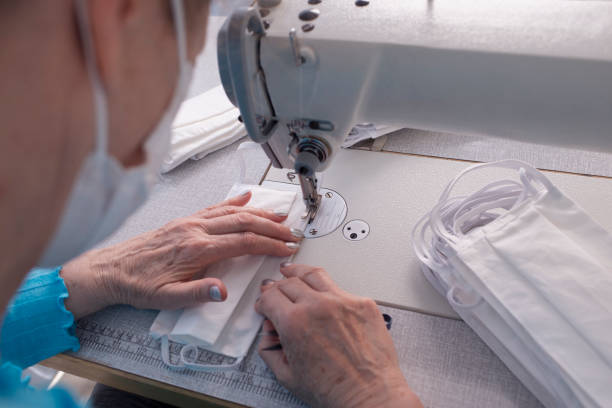 istock Close up image of seamstress's hands stitching fabric, producing face masks. 1221345677