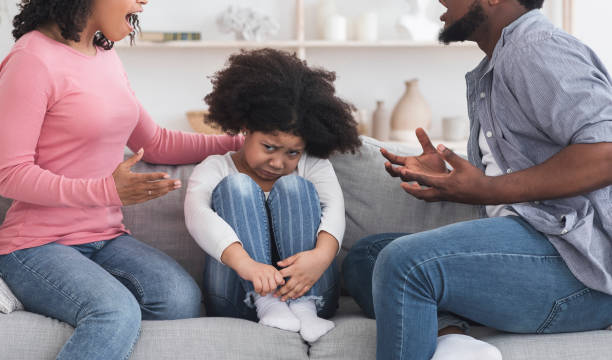 istock Poor Little Black Girl Sitting On Couch Between Quarreling Adults 1221346421