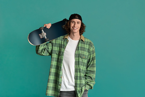 Teenage outdoor activities. Happy young guy holding skateboard on color background