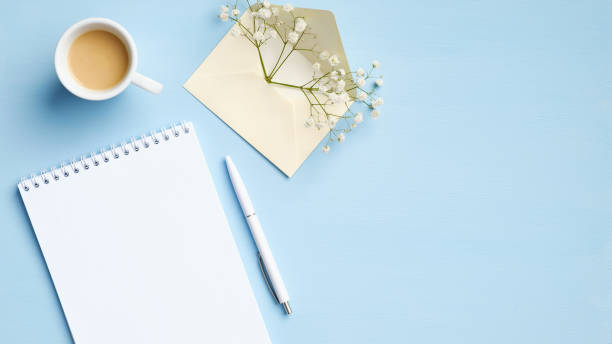 istock Flat lay, top view office table desk with blank paper notebook, cup of coffee, pen and envelope with flowers. Stylish feminine workspace, business concept 1221347297