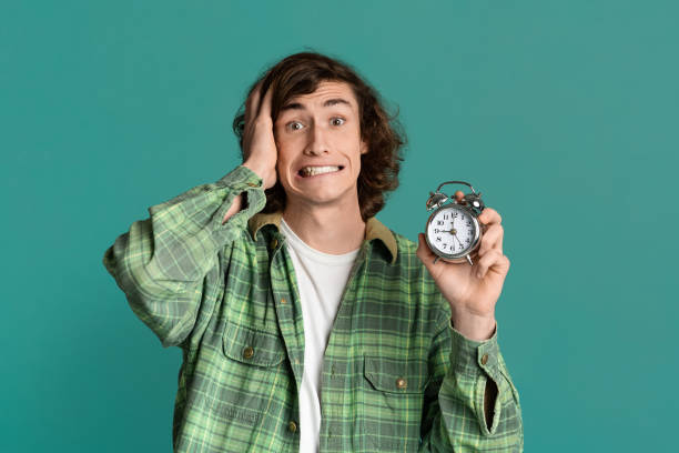 istock Time optimization. Young guy with alarm clock scared of being late on turquoise background 1221347882