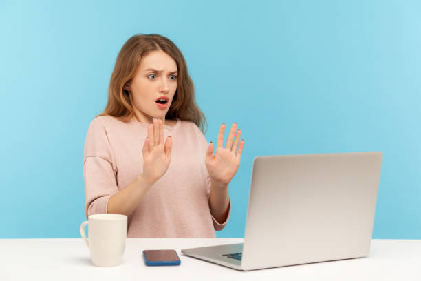 istock I'm scared! Frightened woman with shocked expression raising hands in stop gesture and looking at laptop screen 1221348277