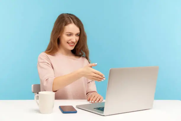 Photo of Online consulting. Happy businesswoman welcoming client with handshake and looking at laptop screen