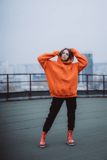 Girl in an orange jacket poses on the roof of a building in the city center stock photo