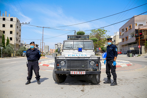 Police officers on duty wearing masks standing by their Jeep in City of Qalqilya, Palestine. a roadblock to enforce movement control order due the coronavirus (Covid-19). Qalqilya, West Bank, Palestinian Territories, Palestine - May 1, 2020