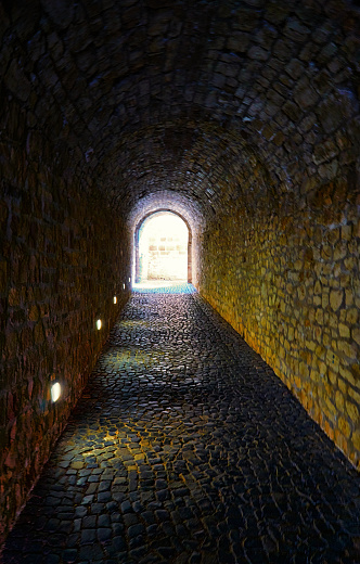 Dark tunnel made of natural stones with light at the end.