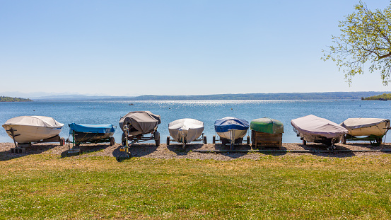 Herrsching, Bavaria / Germany - Apr 22, 2020: Sailboats on land at the shores of Lake Ammer (Ammersee). Lined up in a row. The boats are covered with tarpaulin. Panorama format.