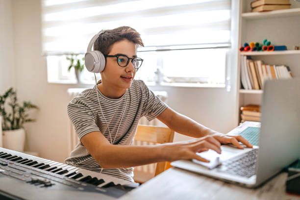 Foto de Young pianist boy looking at the digital tablet screen for learning piano online at home. Music distance learning concept. do Stock