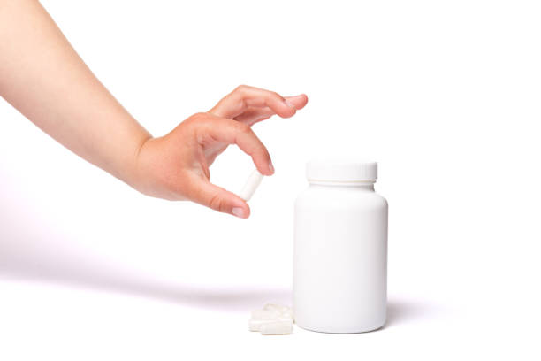 istock Child hand taking vitamins in capsules. Container with no logo and hand taking tablets on a white background 1221362339