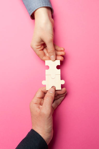 istock Two hands connect puzzles on a pink background. Cooperation and teamwork in business. Collaboration people for success 1221363532
